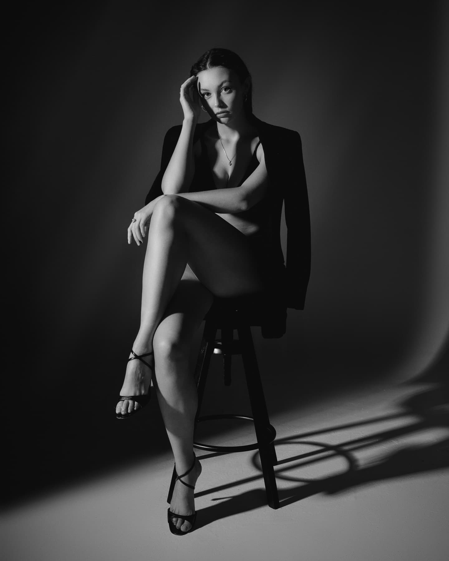 Black-and-white portrait of a model seated on a stool, lit by a hard spotlight