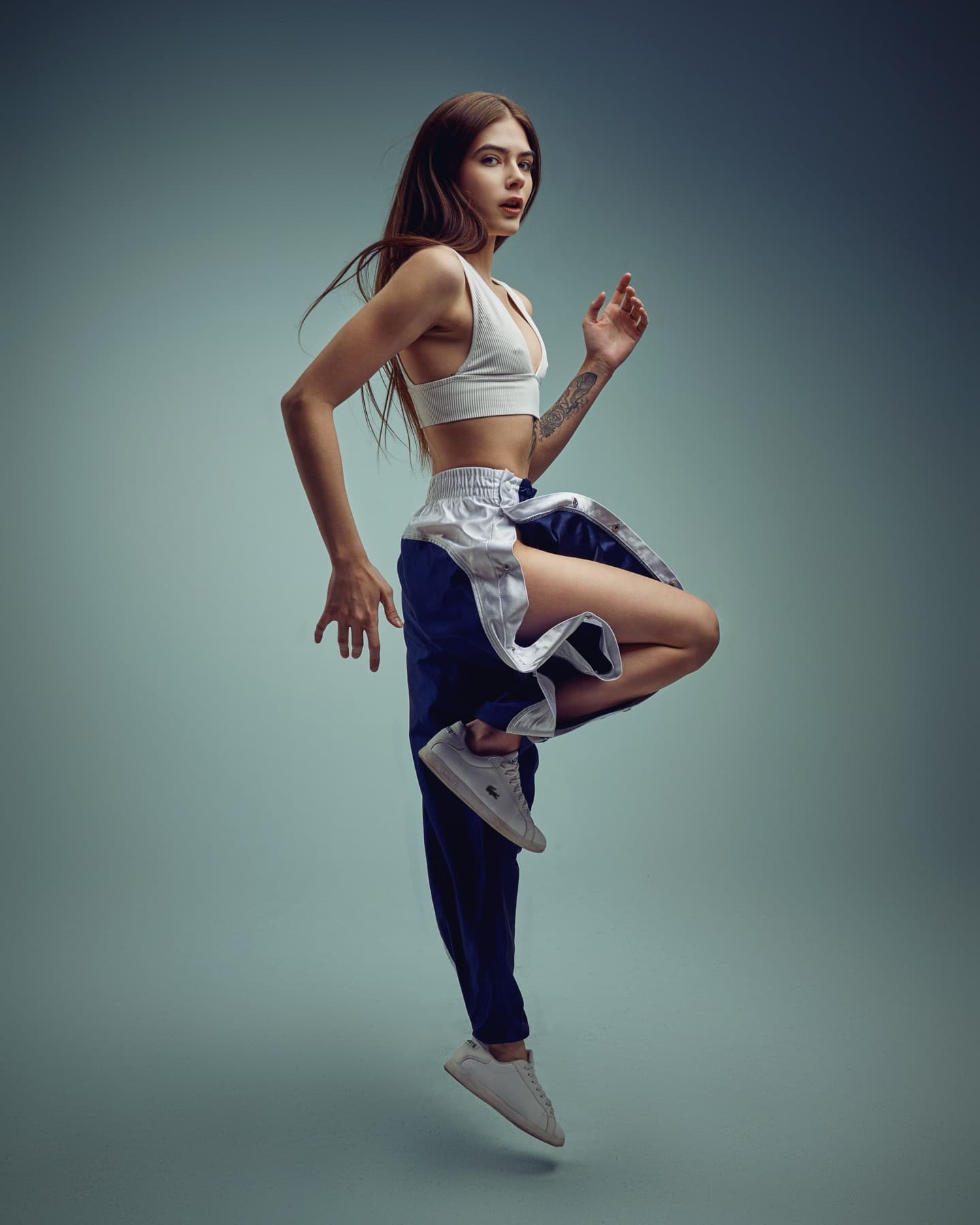 Model mid-jump in a sports bra and track pants against a teal backdrop