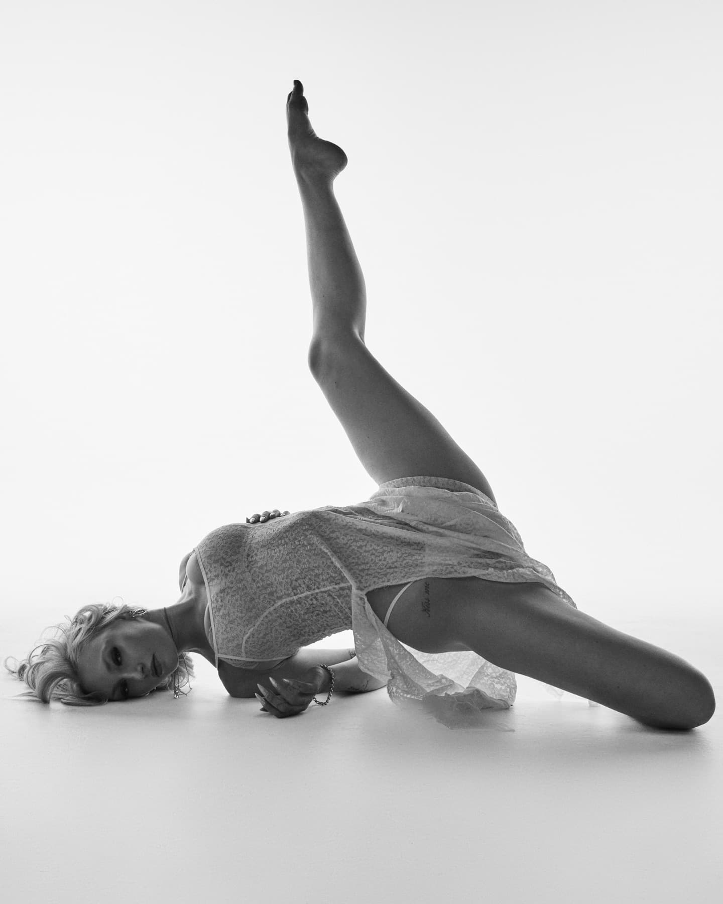 Black-and-white image of a dancer lying on the cyc floor with one leg extended up